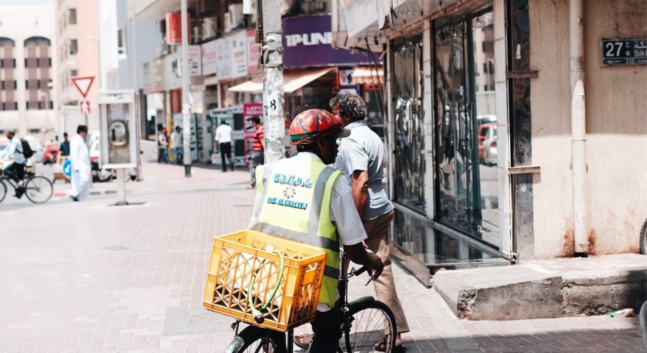 Top 10 Cheap Hotels in Bur Dubai Man rides bicycle with a yellow basket on the back, concrete white buildings in the